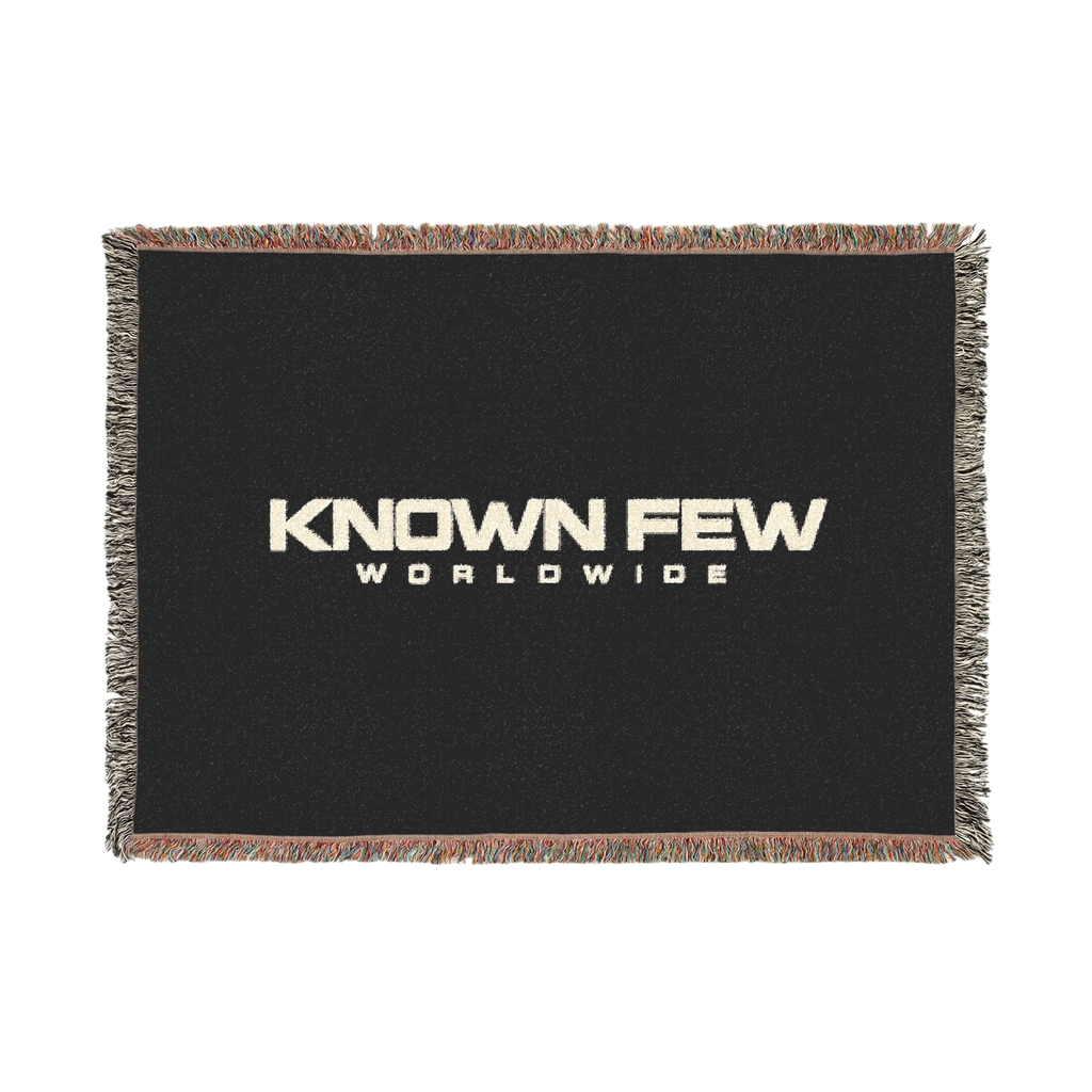 Known Few Worldwide heavyweight cotton blanket in black with a woven logo and colorful fringed edges.