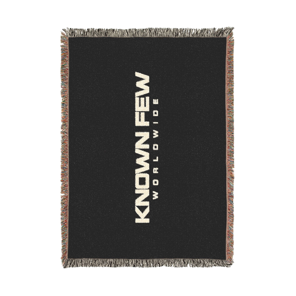 Known Few Worldwide black cotton woven blanket featuring bold white branding and colorful fringed edges.